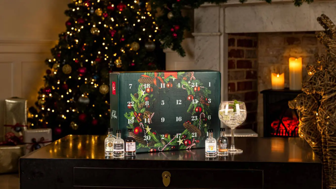 Virgin Wines gin advent calendar next to small bottles of gin and a gin glass in front of a Christmas tree and a fireplace