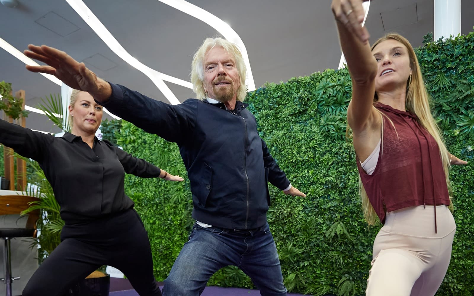 Richard Branson practices yoga with two female instructors in the Virgin Australia lounge