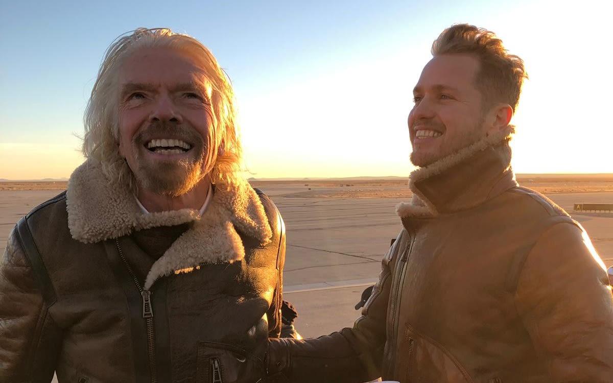 Richard Branson looking into the sky smiling, with Sam Branson at his side, smiling at his dad.
