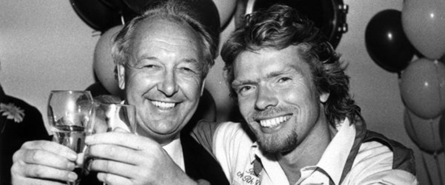 Black and white photo of Richard Branson and Freddie Laker clinking glasses in front of balloons