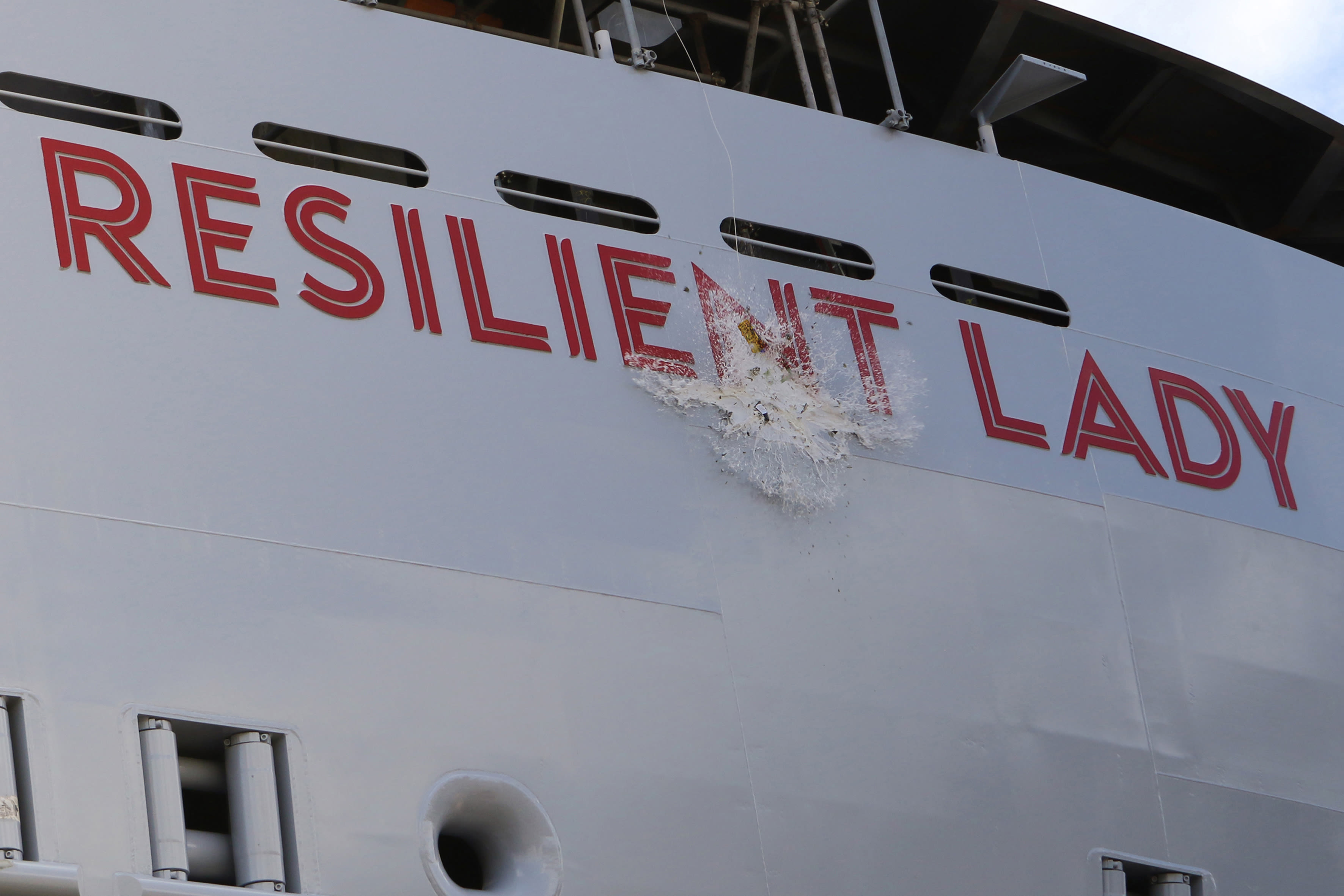 A bottle of champagne smashing on the side of Virgin Voyages' Resilient Lady ship