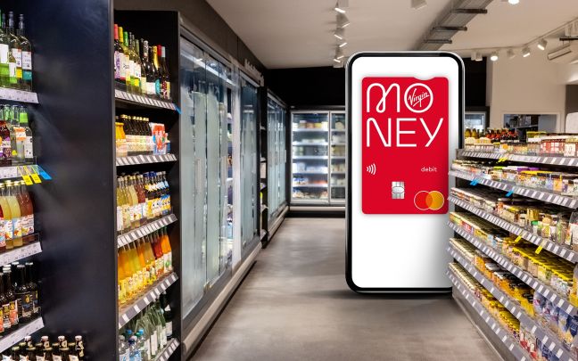 A supermarket aisle with an oversized smartphone showing a Virgin Money debit card