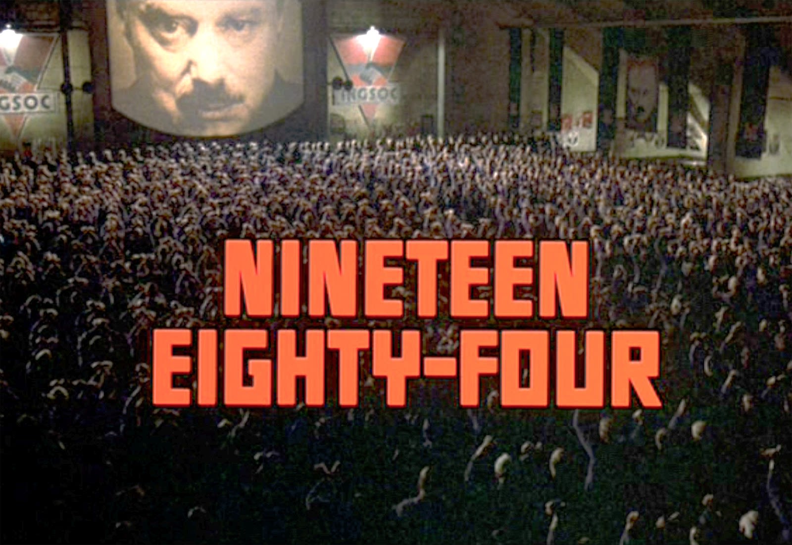 Scene from 1984 the film where hundreds of people are gathered, 'Nineteen Eight-Four' written in red capital letters across the screen