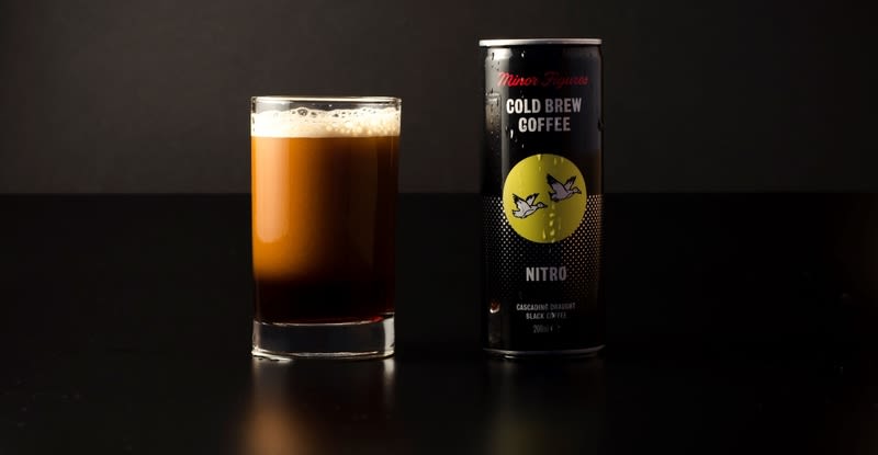 A glass with cold brew coffee in, next to a can of Minor Figures cold brew coffee