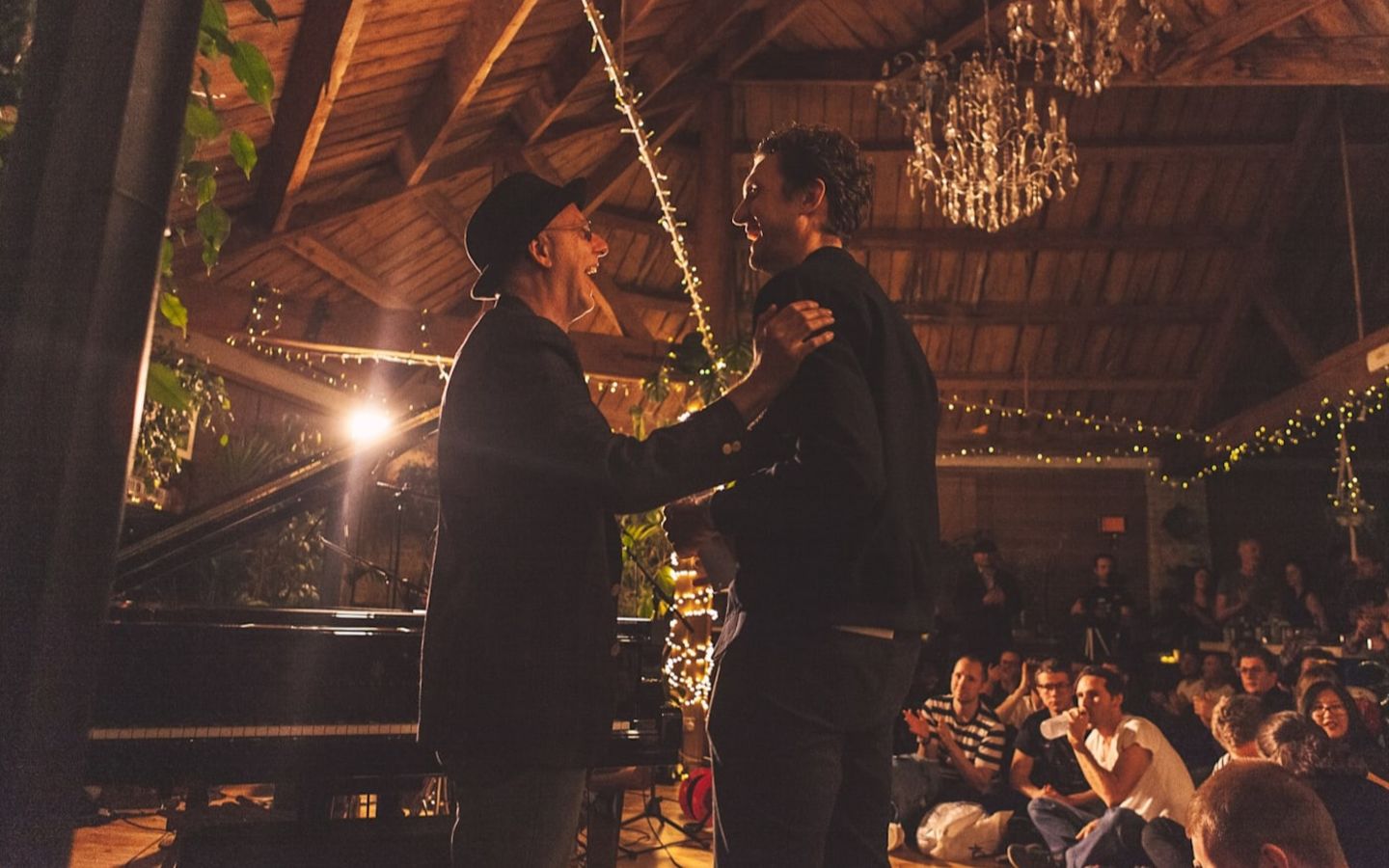 Rafe Offer and Dave Alexander laughing together on stage next to a piano, in front of an audience