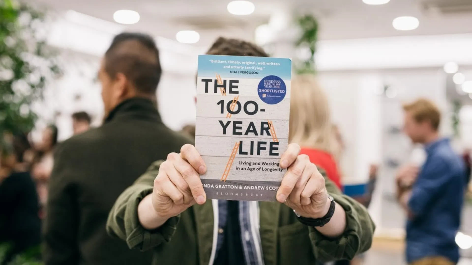 A person holding a copy of the Book The 100-Year Life to the camera