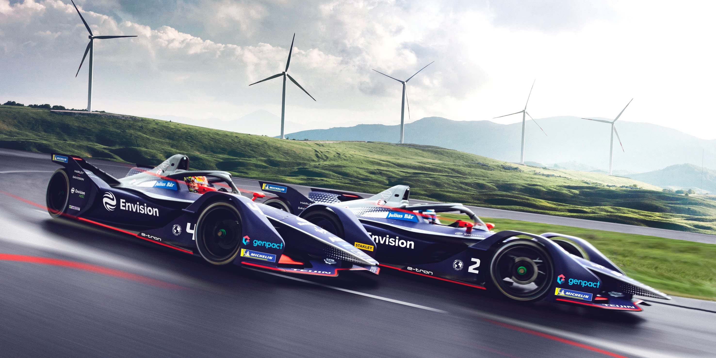 Two Envision Virgin Racing cars with wind turbines in the background
