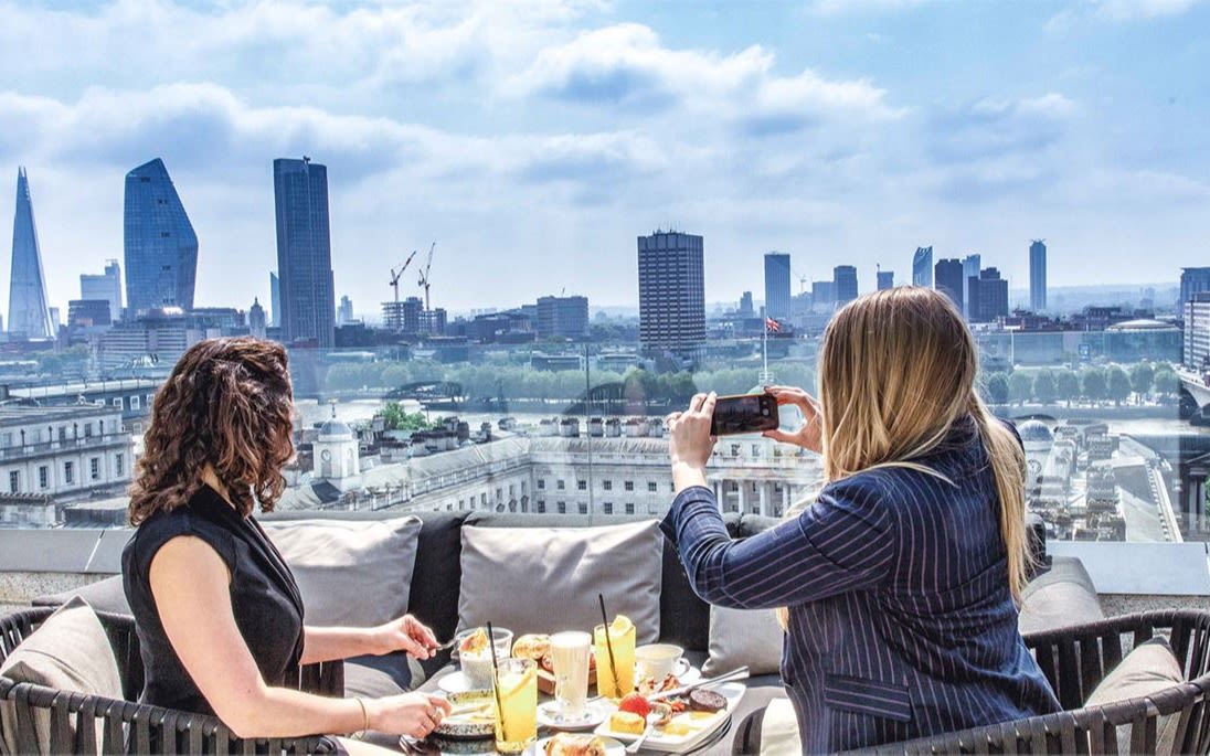 Image of two ladies dining at Radio Rooftop whilst taking pictures of the London skyline.