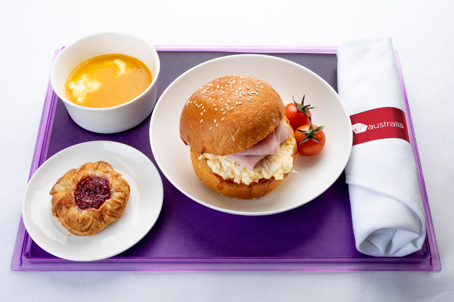 Ham and scrambled egg brioche roll with tomato relish, served alongside Greek yoghurt with mango coulis and seasonal fresh fruit Business Class offering Virgin Australia