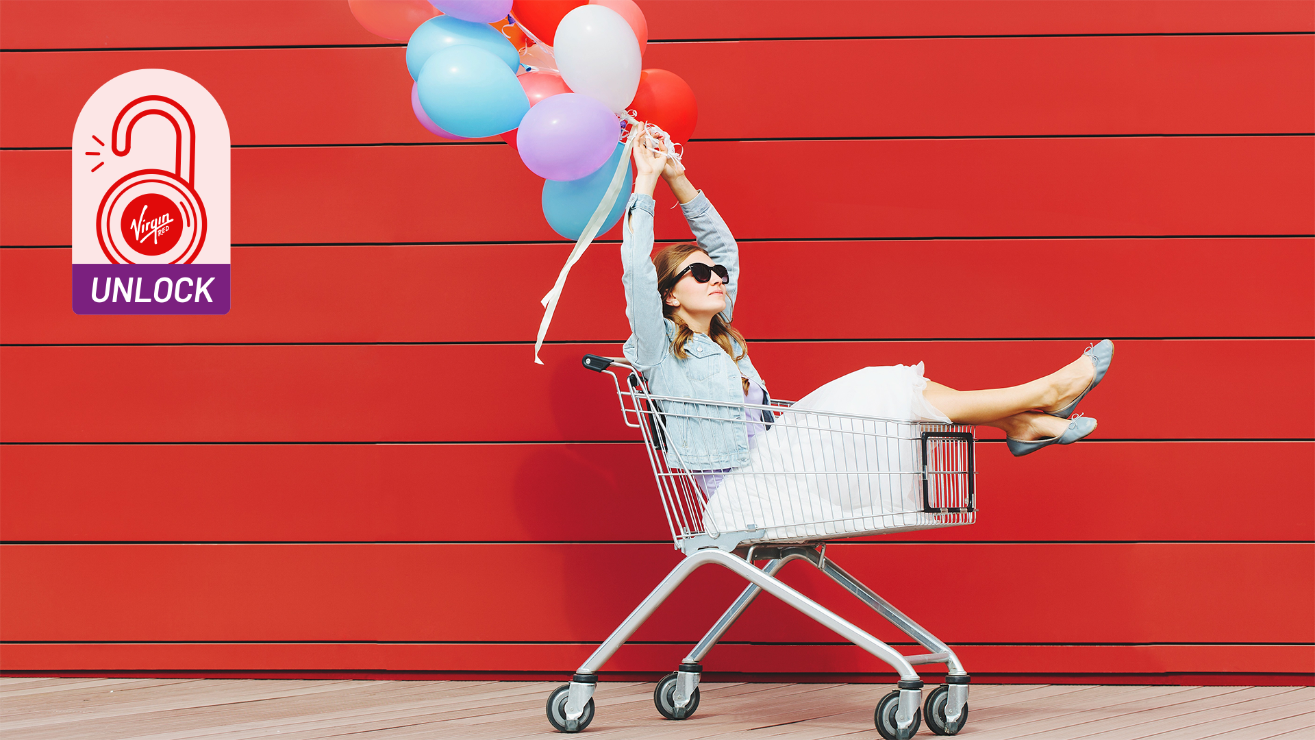 Image of a lady in a shopping trolley with balloons, very pleased about her purchases.