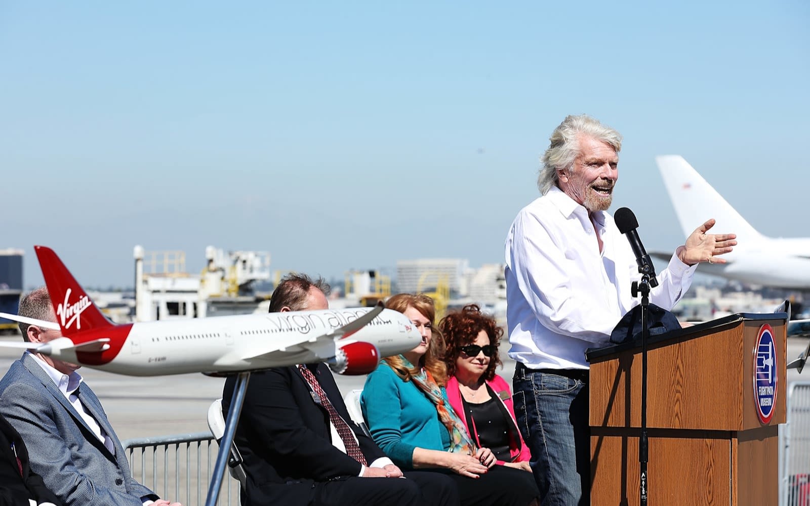Richard Branson talking at Los Angeles Airport at a podium in front of a panel