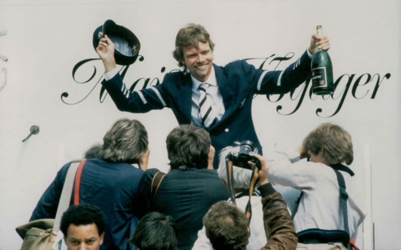 Richard Branson celebrates the inaugural Virgin Atlantic flight with champagne in front of photographers