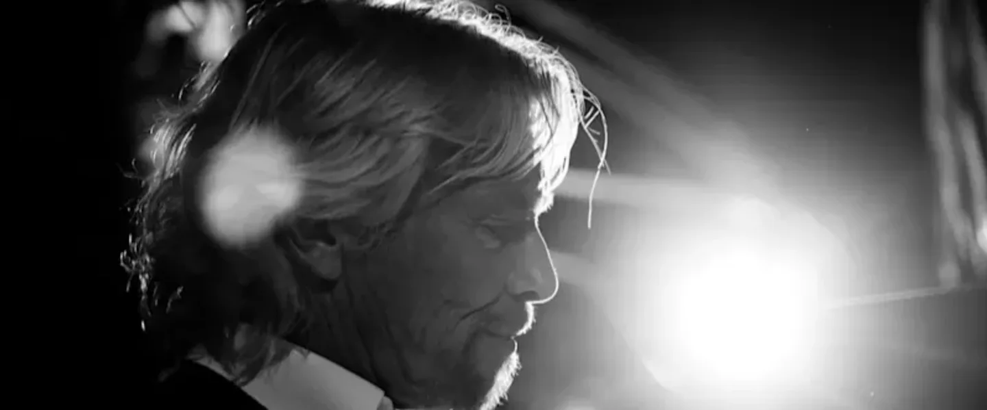 Side profile black and white photo of Richard Branson looking serious with a bright light behind him