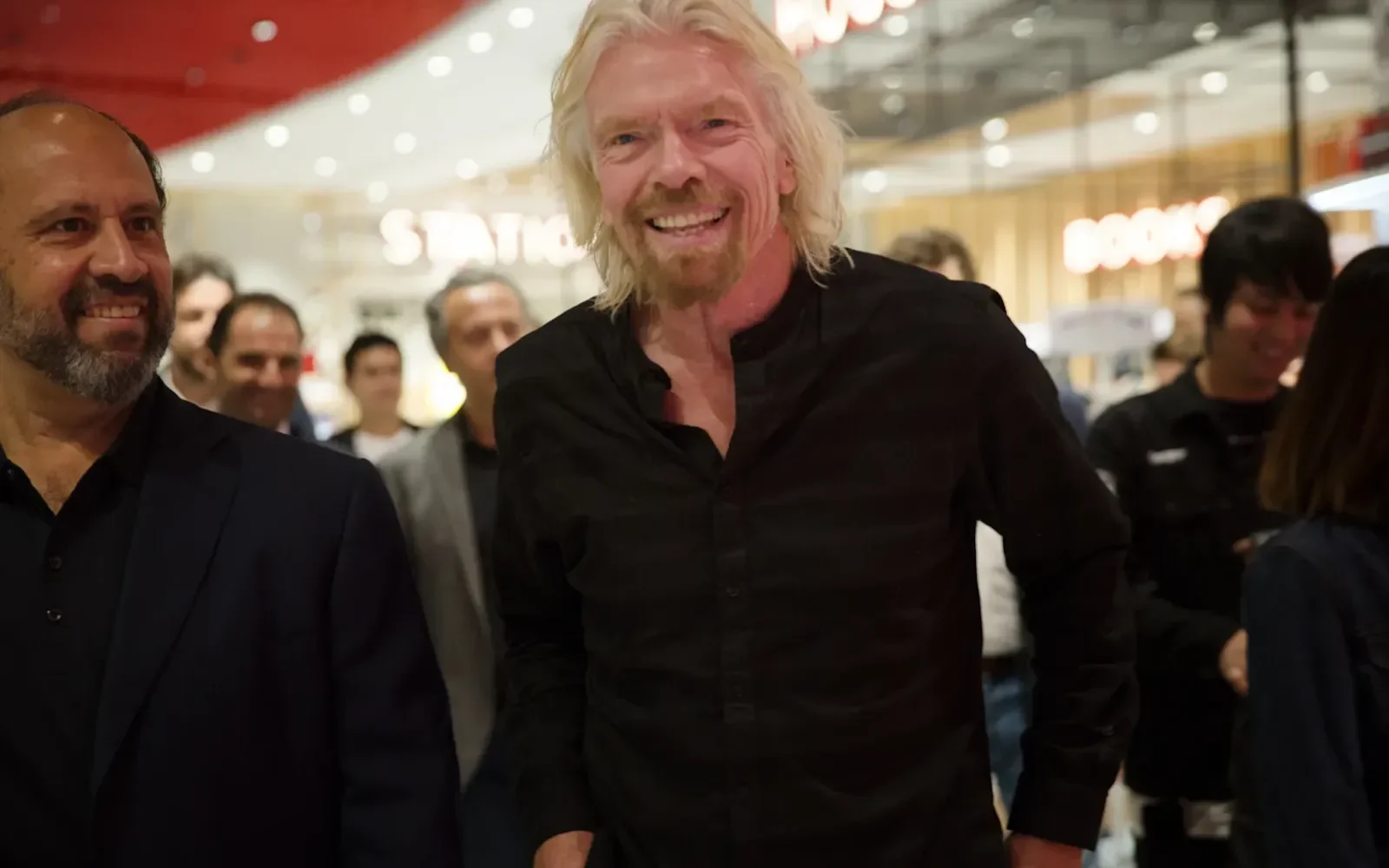 Richard Branson smiling at the camera, surrounded by a crowd of people 