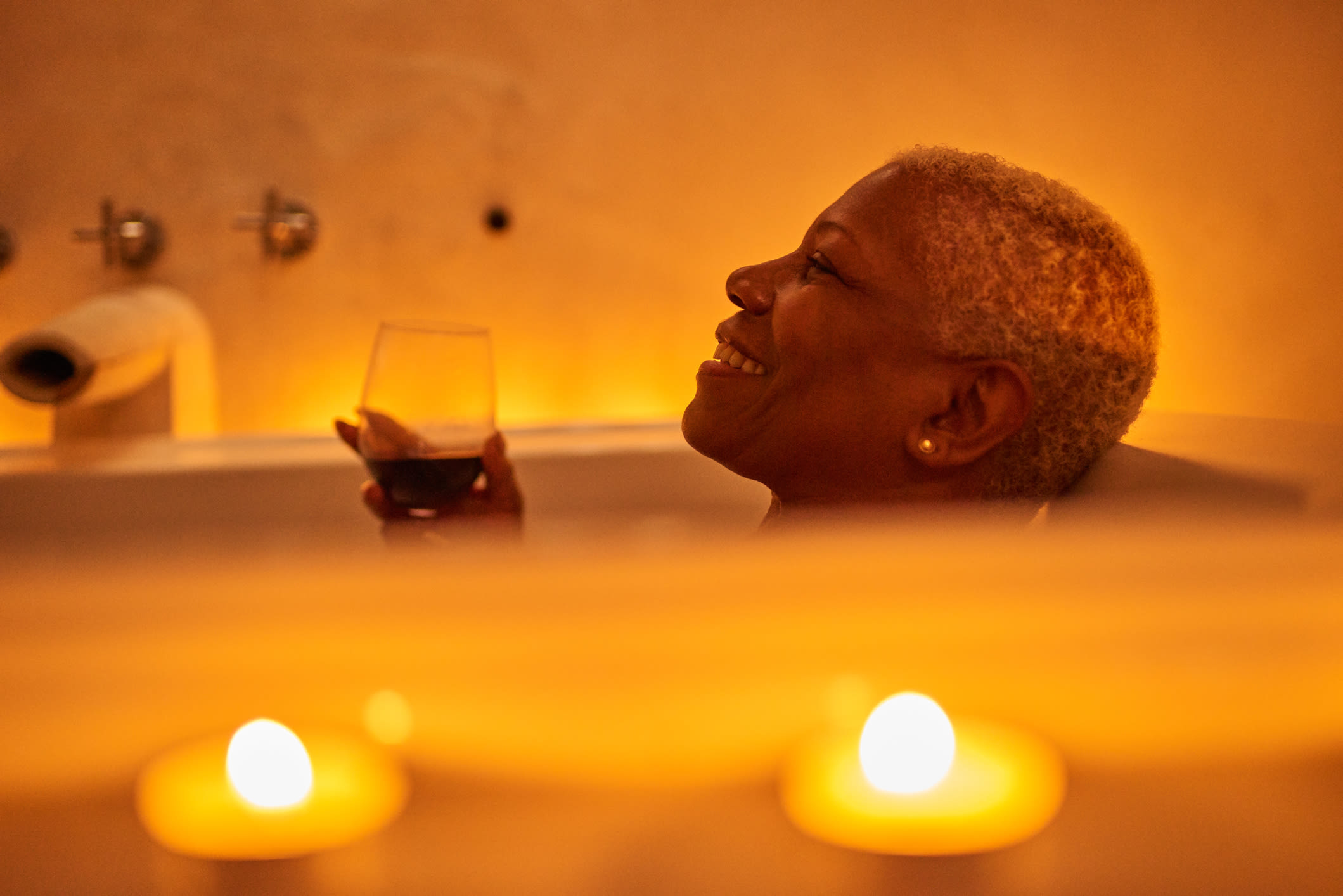 A woman relaxing in a bath with a glass of wine and candles