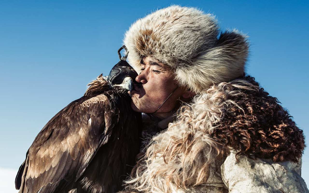 A Mongolian man holding an eagle kissing its beak