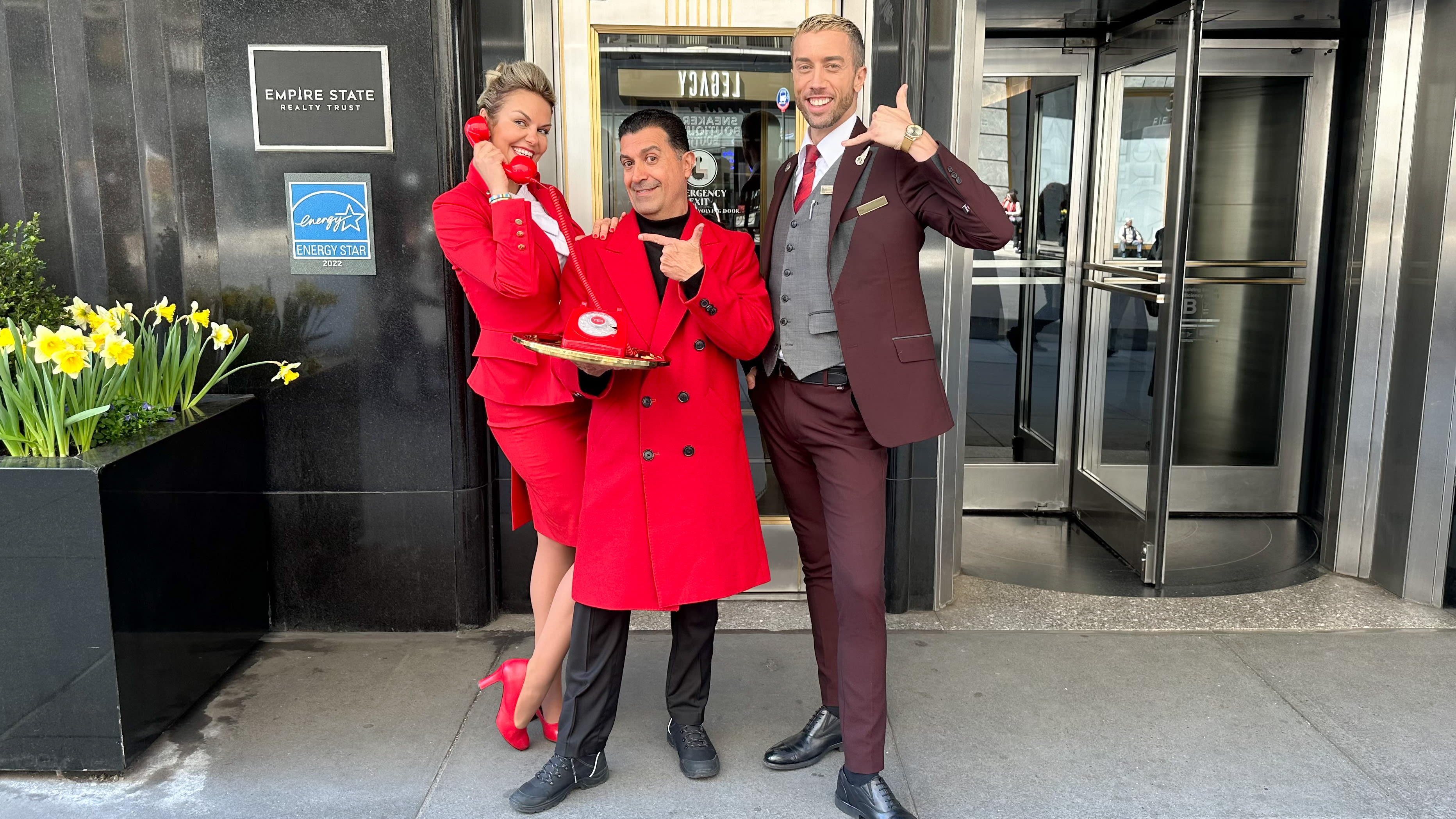 Two Virgin Atlantic cabin crew and one Virgin Hotels doorman stood outside the Empire State building holding a red phone with the words "YES" on a gold tray