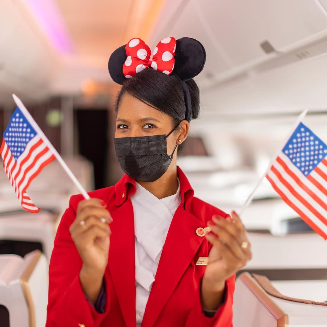 Virgin Atlantic cabin crew wearing Minnie Mouse ears, holding two USA flags