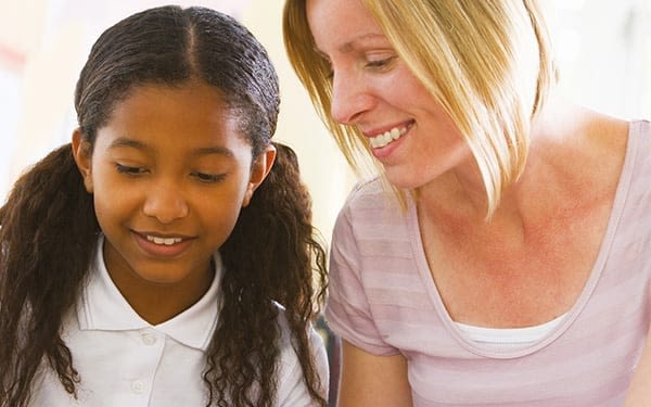 A caregiver sits beside a child as they work on a laptop together