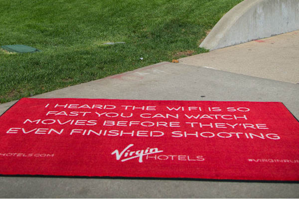 Red Virgin Hotels doormat that reads: "I heard the WiFi is so fast you can watch movies before they're ever finished shooting."