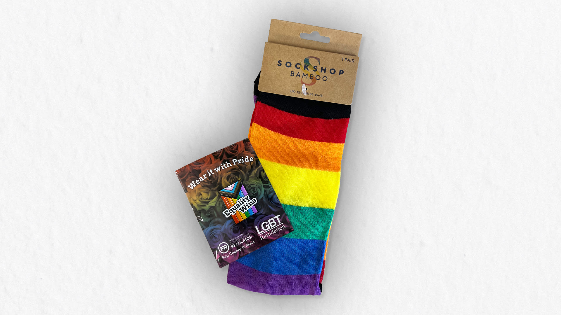 Image of a pair of Pride socks (red, orange, yellow, green, blue and purple) and a wear it with pride badge from LGBT Foundation.