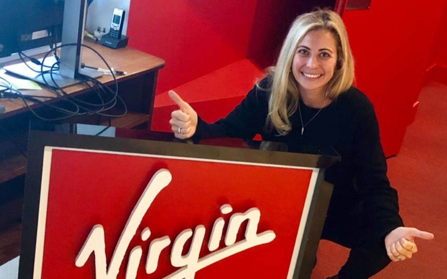 Holly Branson at the Virgin Management office in London - smiling in front of a Virgin logo