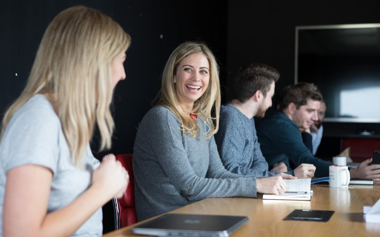 Holly Branson sitting at a desk with four other people laughing with a lady sitting next to her 