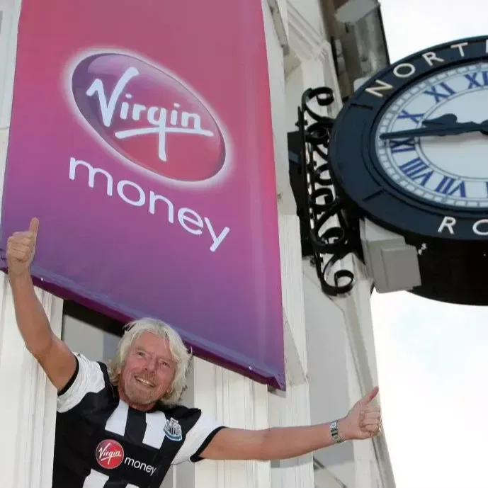 Richard Branson in a Newcastle football shirt gives a thumbs up from a window