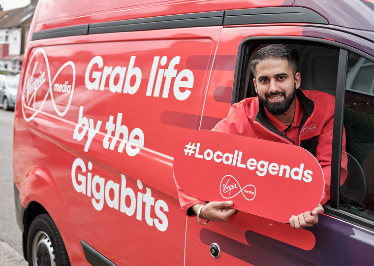 A Virgin Media engineer leans out of the window of his van, holding a sign that reads "#LocalLegends"