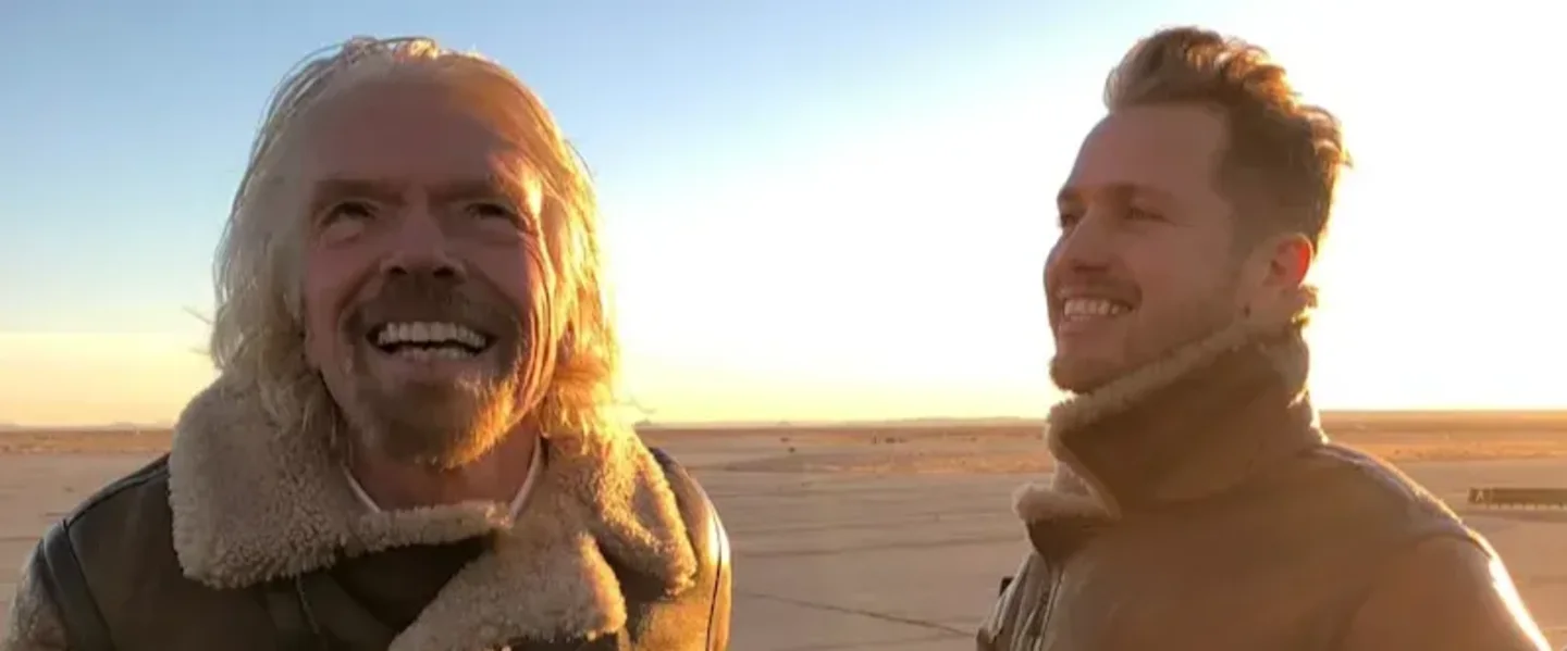 Richard Branson looks up at the sky smiling, while son Sam Branson looks at him and smiles