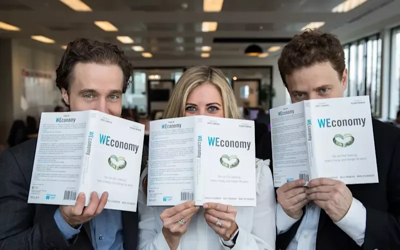 Holly Branson with Marc and Craig Kielburger, holding copies of WEconomy in front of their faces