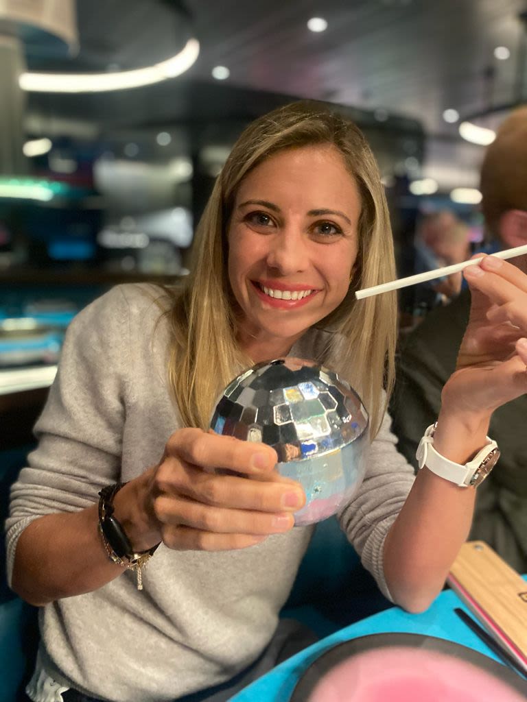 Holly Branson smiles while holding a disco ball drink on Virgin Voyages' Summer Soiree sail