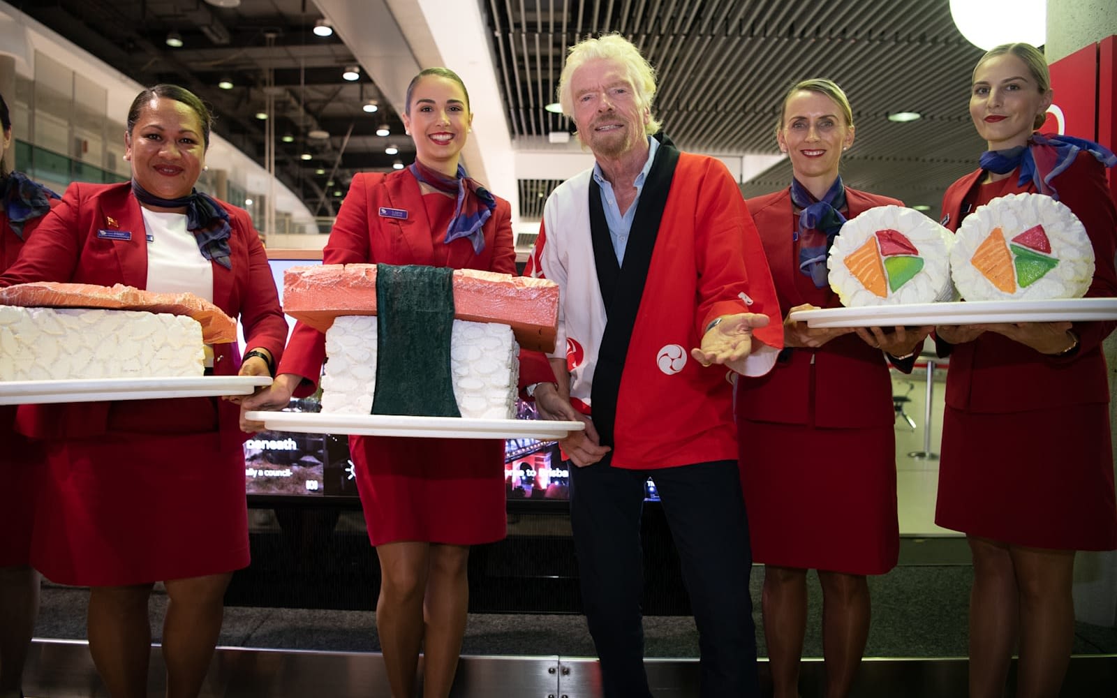 Richard Branson poses with Virgin Australia cabin crew carrying giant sushi to celebrate the launch of flights to Tokyo