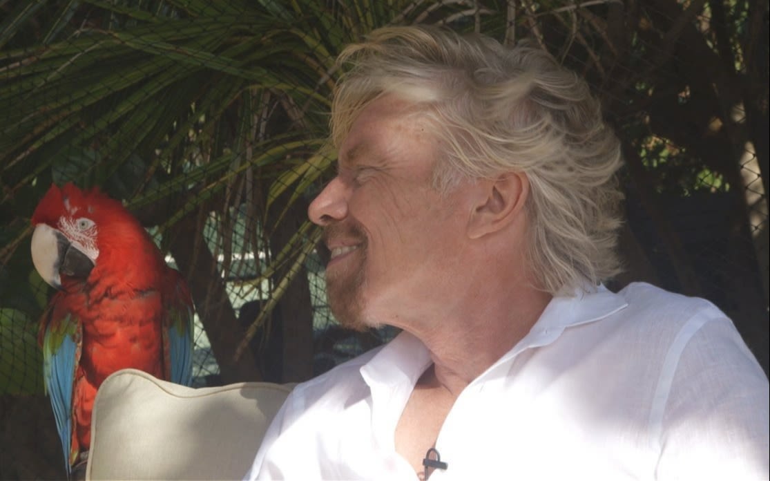 Richard Branson sitting next to a parrot