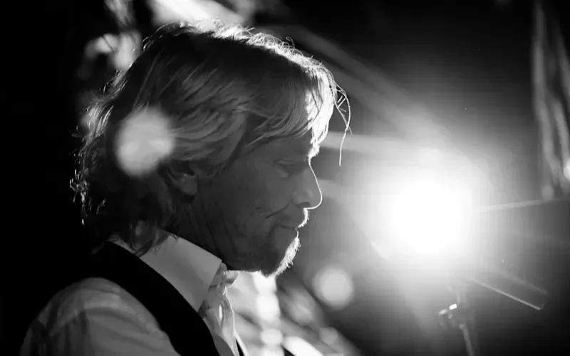 A black and white photo of Richard Branson. Side profile view, he has a serious face