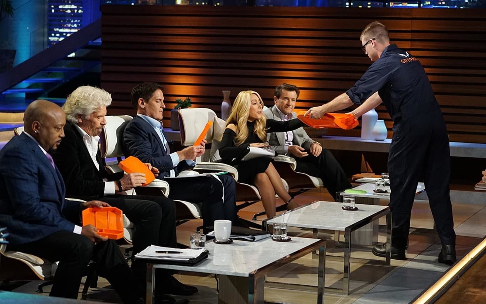 Richard Branson sitting on the Shark Tank judging panel. A contestant is handing out a product to the judges.