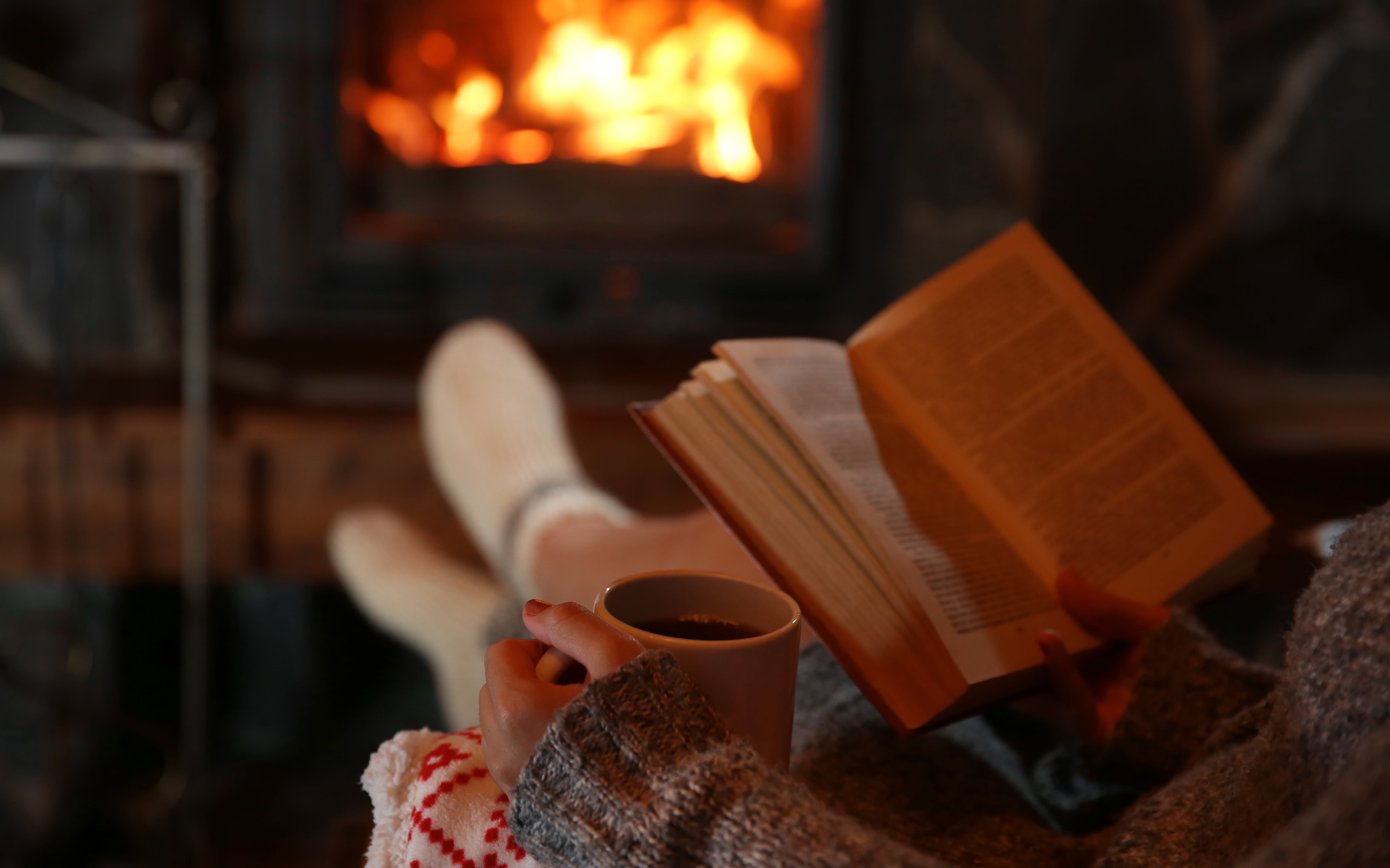 Woman enjoys book near a fire with a hot drink