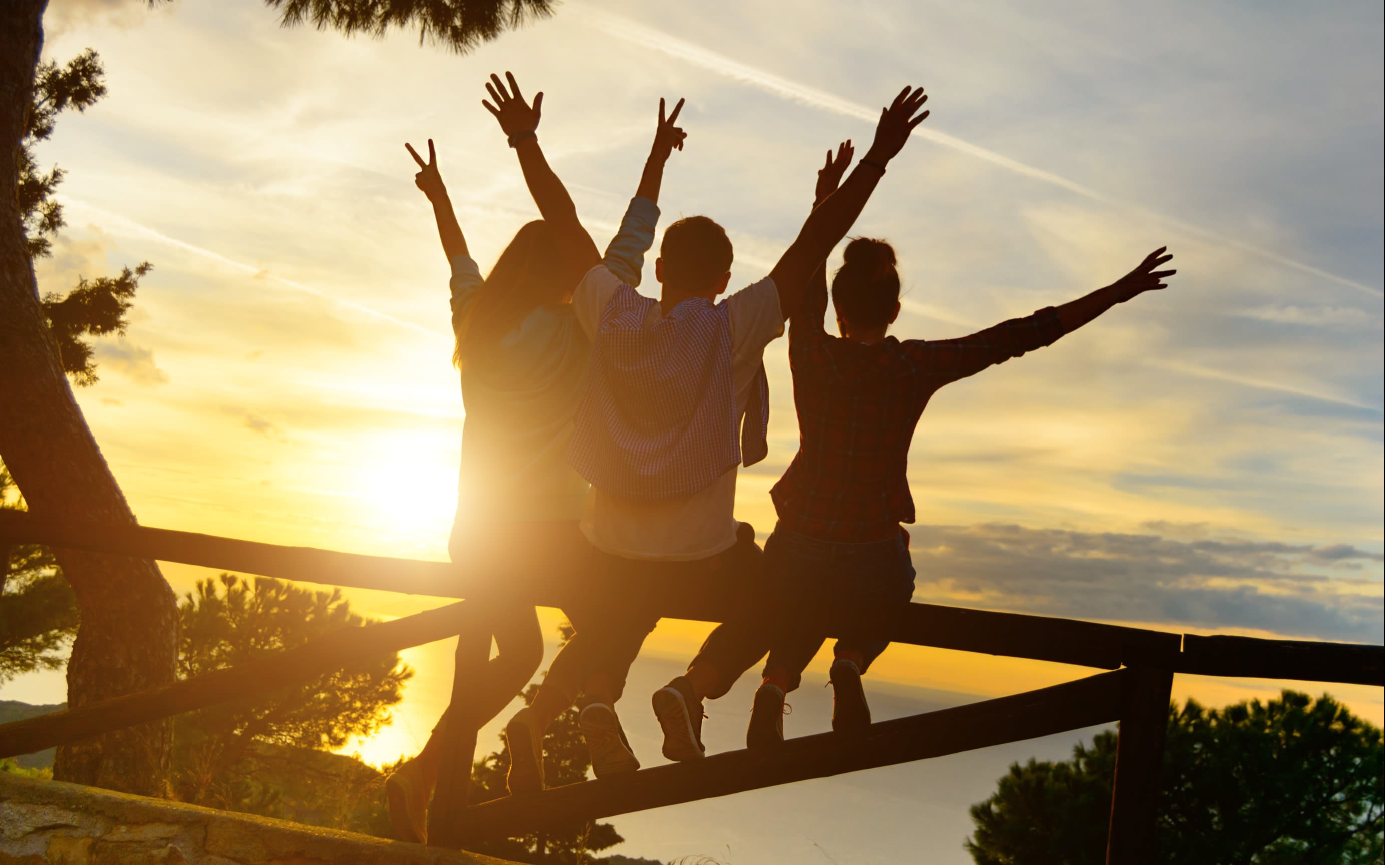 Rear view of three best friends travellers putting their hands up at sunset. 