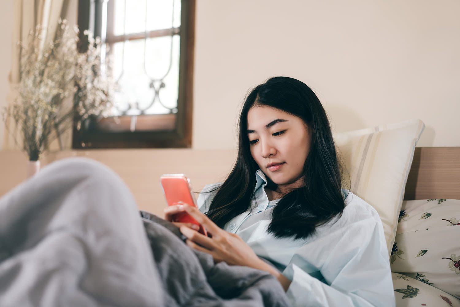 A young woman sitting on her bed looking at her phone