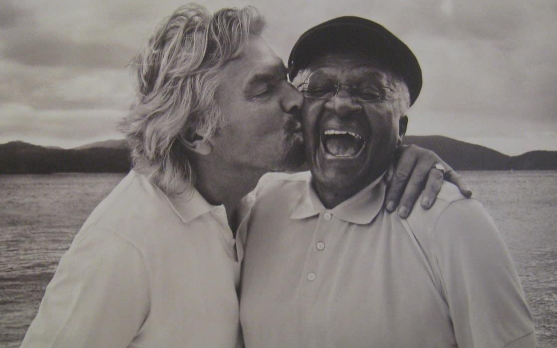 Richard Branson kissing a man on the cheek who's laughing