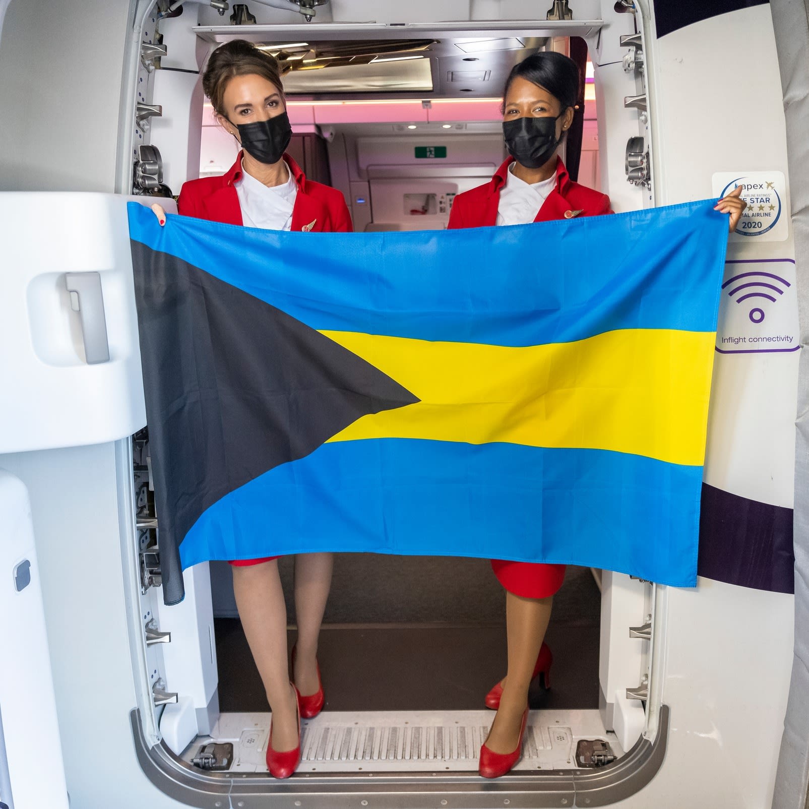 Two Virgin Atlantic cabin crew members hold a Bahamas flag