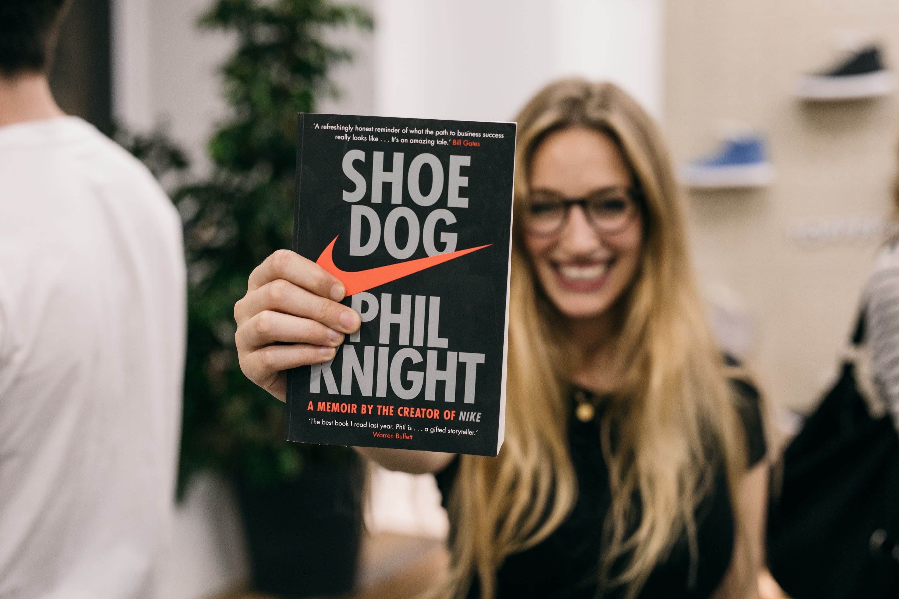 A woman holding a copy of thee book Shoe Dog by Phil Knight
