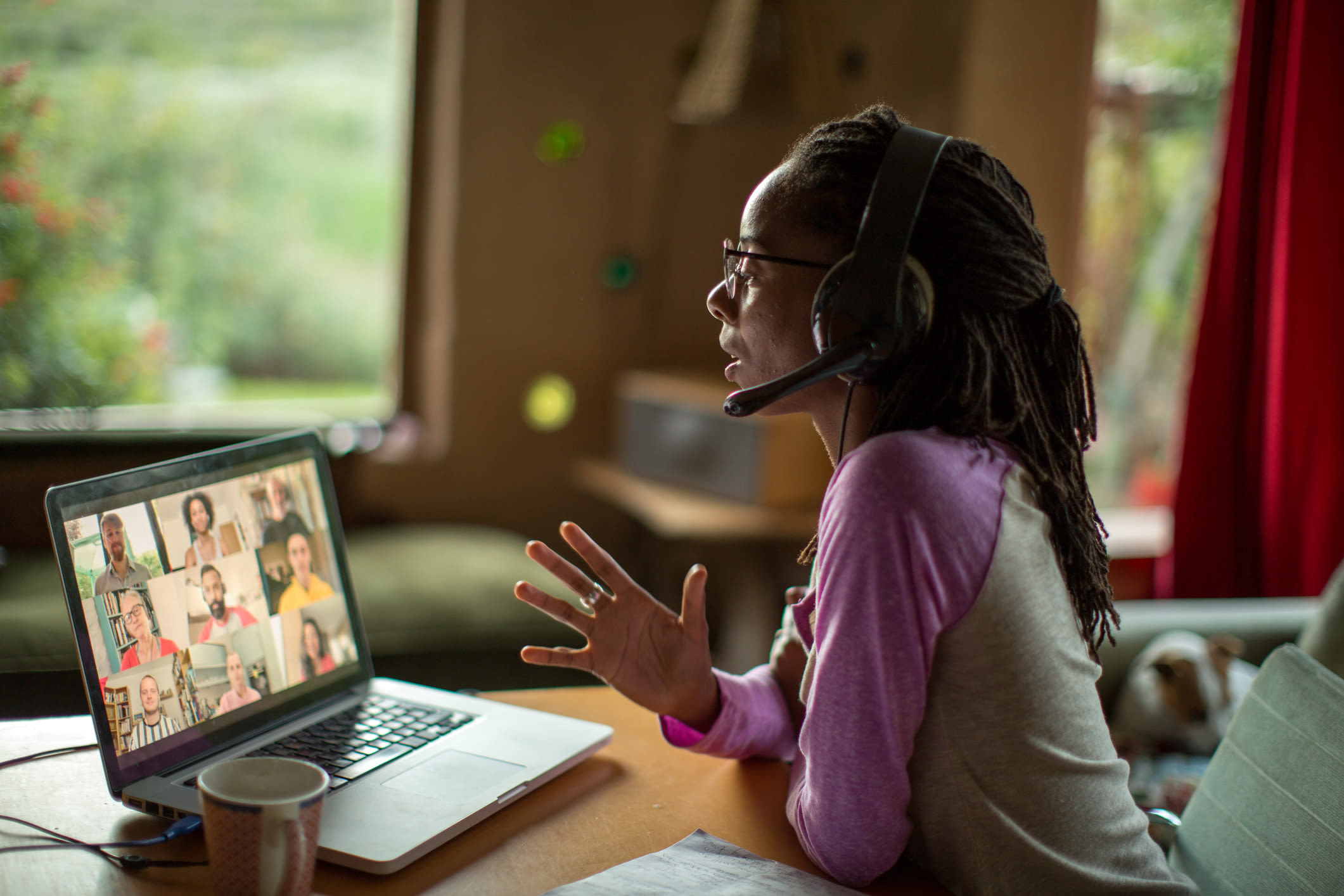 A Black woman wears a headset while on a video call with nine other people on her laptop