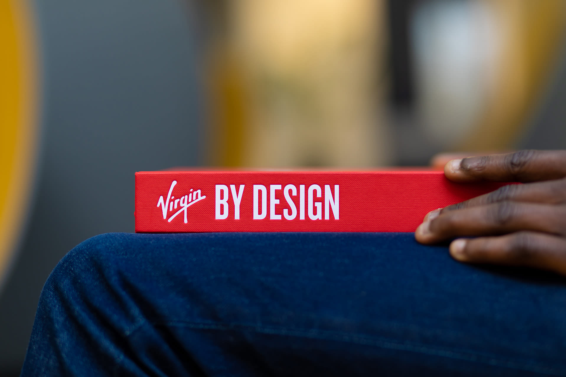 'Virgin by Design' book on someone's knee, just the spine is visible. It is a red cover with the title in white.