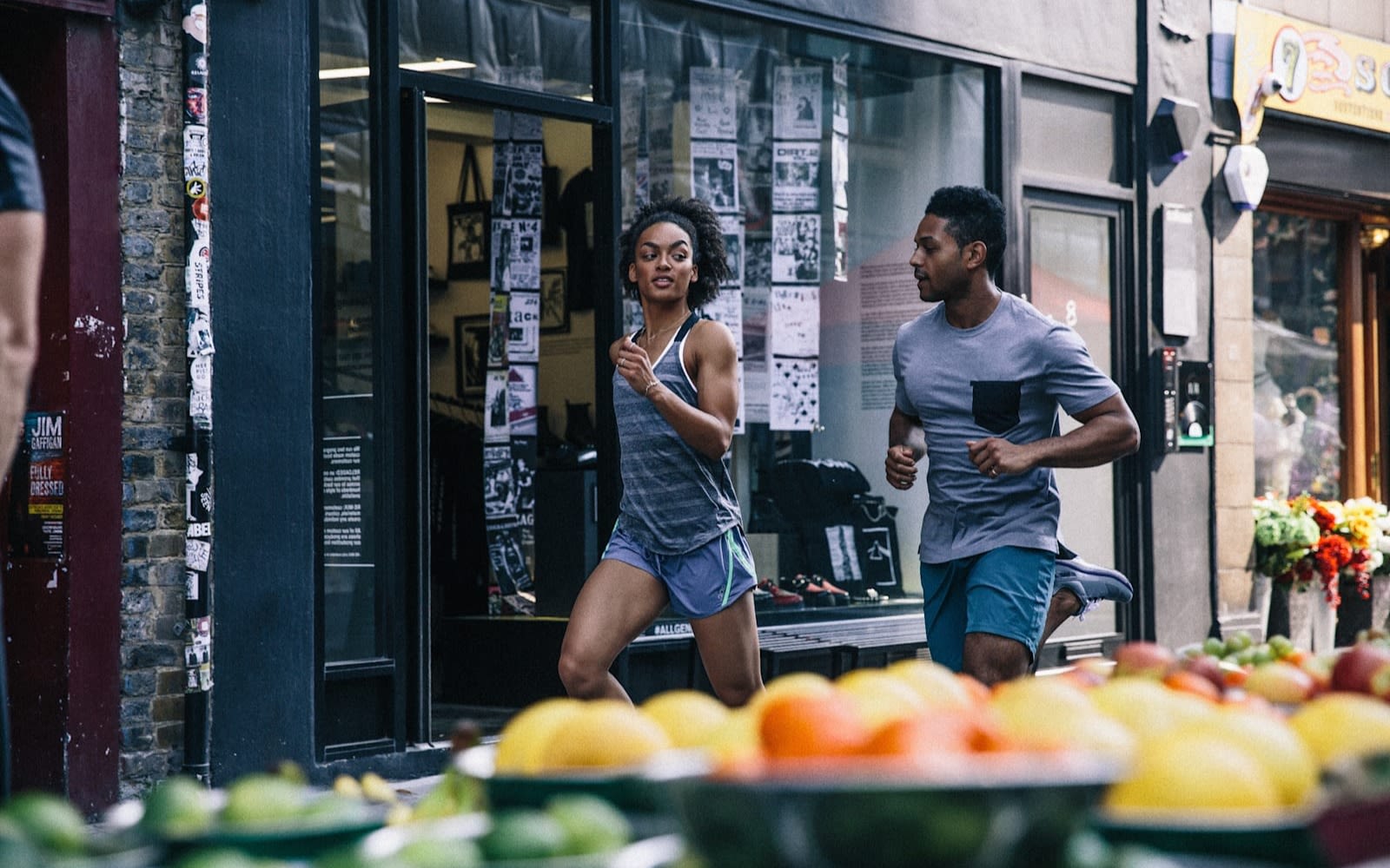 Two people run through an urban street that is hosting a market