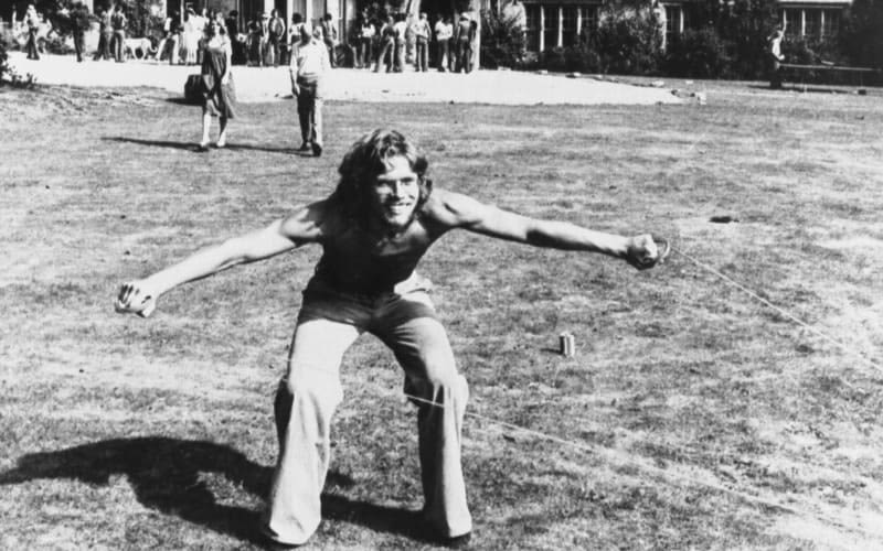 A black and white picture of young Richard Branson smiling and arms open wide, in a field.