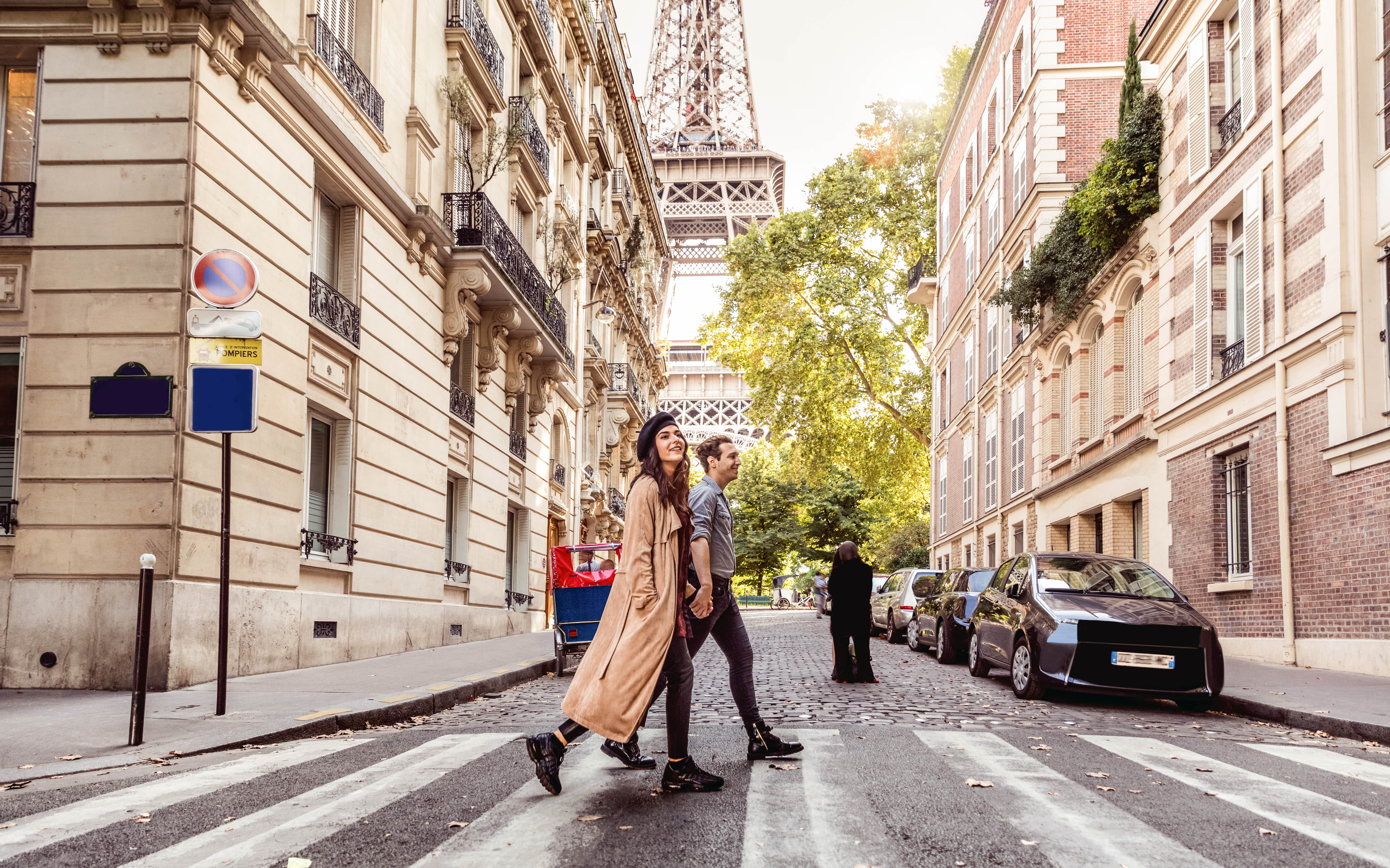 Image of two people crossing a road in Paris with the Eiffel Tower in the background.