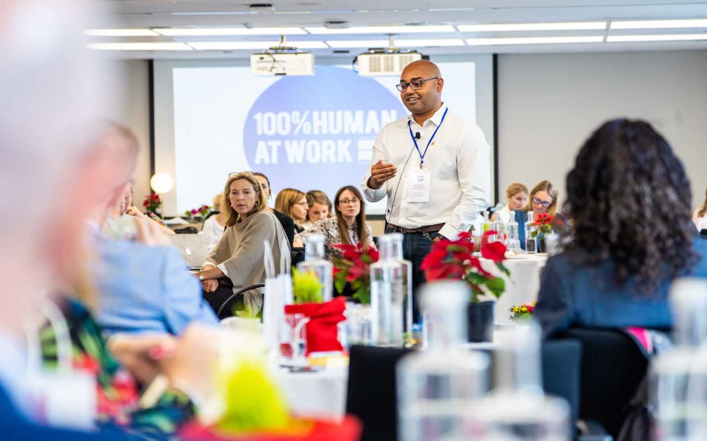 Man stood up giving a speech to people sat around him