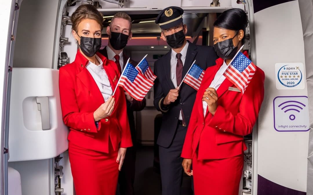 Virgin Atlantic cabin crew and pilot stand at the door of an aircraft waving US flags