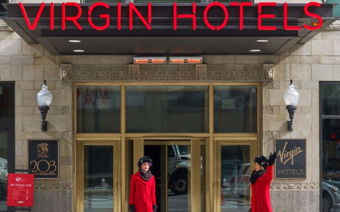 The exterior entrance to Virgin Hotels Chicago. Two women in red coats are standing outside, one is hailing a taxi